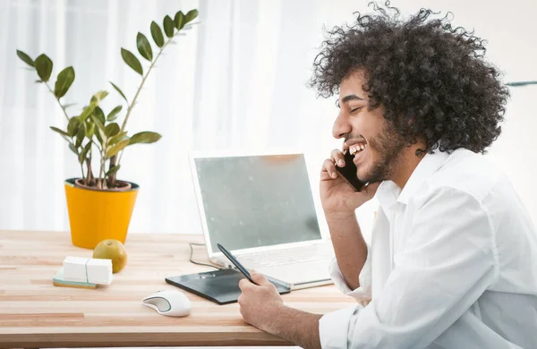 Homem criativo se comunica por telefone celular sorrindo enquanto sentado no local de trabalho em casa. Conceito freelance. Trabalho a partir do conceito de casa. Vista lateral. Copie o espaço do lado esquerdo. Imagem tonificada — Fotografia de Stock