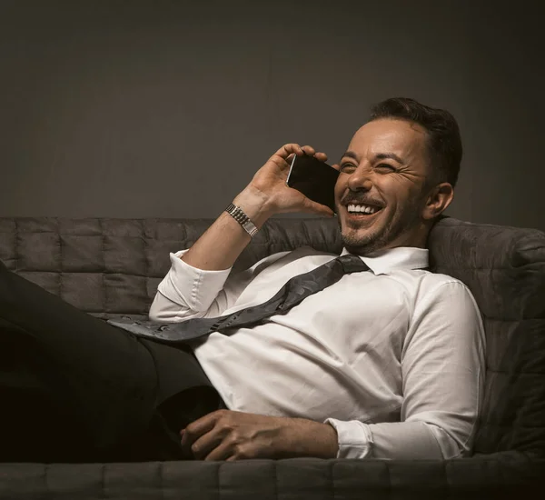 Happy Businessman tersenyum di ponsel. Pria muda berseragam Kaukasia telah berkomunikasi di sofa di kantor perusahaan. Konsep beristirahat. Citra berdada — Stok Foto