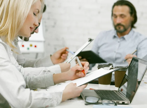 Business team brainstorming in office. Colleagues works sitting at office table with laptop and coffee cups on it. Selective focus on business woman writing by red marker on paper sheet in foreground — Stock Photo, Image