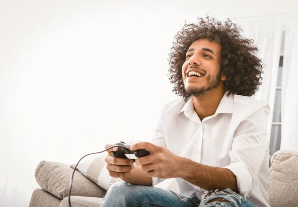 Homem feliz a jogar jogos de computador. Jovem árabe entretém em casa em auto-isolamento durante a quarentena. Copie o espaço do lado esquerdo. Imagem tonificada — Fotografia de Stock