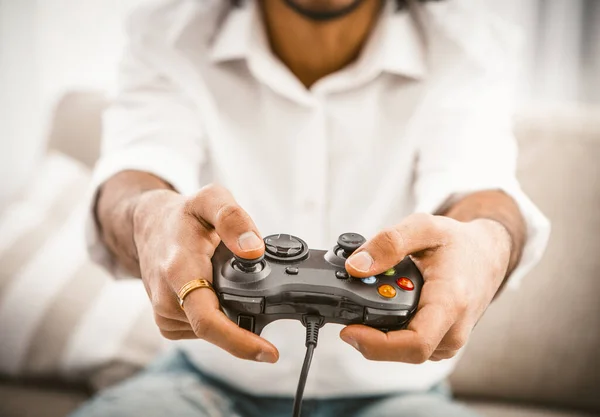 Ο ανοιχτόχρωμος κουνάει τα κουμπιά. Νεαρός άνδρας με λευκό πουκάμισο χρησιμοποιεί ενσύρματο gamepad ενώ παίζει ηλεκτρονικό παιχνίδι. Παίζοντας αντρική ιδέα. Κοντινό πλάνο. Τονισμένη εικόνα — Φωτογραφία Αρχείου