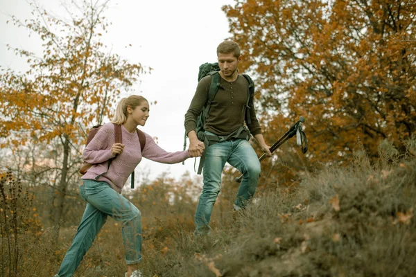 Liefhebbend stel toeristen beklimmen de helling hand in hand. Vrolijk jong stel, man en vrouw met rugzakken reizen samen in de herfstnatuur. Wandelconcept. Gezond levensstijl concept — Stockfoto