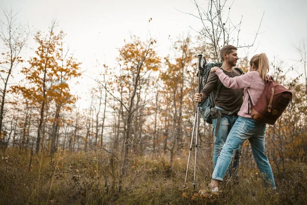 Couple of tourists in love stands embracing leaning on hiking sticks. Young Caucasian man and woman on the background of a young autumn forest. Support concept — Stock Photo, Image