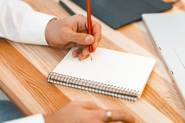 Een jonge creatieve man die aantekeningen of schetsen maakt van een nieuw project per pensil in het notitieboekje. Planning concept. Dichtbij schot. Getinte afbeelding — Stockfoto