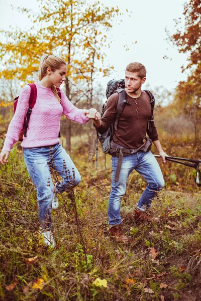 Toeristen in liefde wandelen in de herfst de natuur hand in hand. Twee jonge backpackers, man en vrouw gekleed in warme kleren, waden voorzichtig door dik gras met wandelstokken in de hand. Reisconcept — Stockfoto