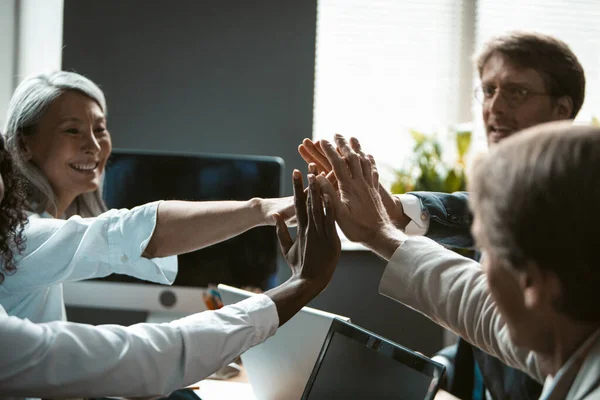 Teamarbeit oder Brainstorming. Multinationale Gruppe von Büroangestellten schlossen sich zu einer Einheit zusammen und gaben einander freudig eine High-Five-Geste — Stockfoto