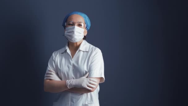 Médico positivo ou enfermeiro de uniforme protetor fica de braços cruzados em fundo azul. Médica branca olha para a câmara. Espaço de texto ou espaço de cópia no lado esquerdo — Vídeo de Stock