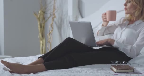 Empresária trabalhando em laptop goza de uma xícara de café quente ou chá antes de trabalhar até tarde da noite recebendo trabalho feito. Mulher de negócios relaxa na cama depois de um longo voo. Conceito de negócio. Prores 422 — Vídeo de Stock