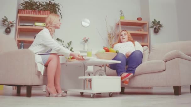 Nutritionist doctor talking to oversized problem girl discussing healthy food benefits and consults about health issues. Healthy food concept. Tinted video. Low side view. Prores 422 — Stock Video