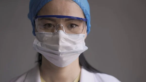 Médico cansado em fundo cinza. Mulher asiática a olhar para a câmara. Imagem abstrata desfocada em movimento — Fotografia de Stock