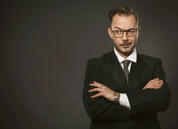 Confident businessman cunningly looks away with his arms crossed. Caucasian middle-aged man standing against a gray wall with copyspace or space for text on the left. Toned image — Stock Photo, Image