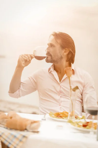 Vit man dricker lyxvin utomhus. Profil bild av attraktiv medelålders man njuter av underbar dryck medan du sitter i sommar café på bakgrunden av havet i naturen. Tonad bild — Stockfoto