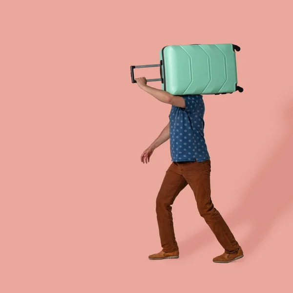 L'uomo porta un bagaglio valigia di plastica sulla spalla andando su sfondo rosa. L'uomo caucasico di mezza età con indosso abiti casual va in viaggio d'affari. Concetto di viaggio — Foto Stock