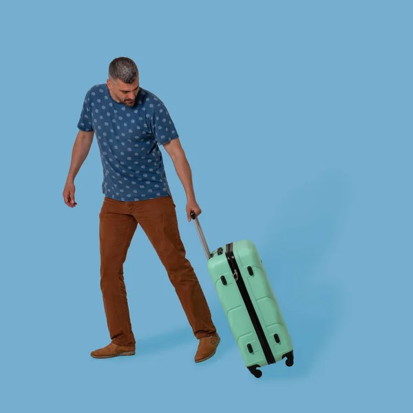L'uomo porta la valigia di plastica che lo tiene piegando la maniglia. Tagliare su sfondo blu. Un bell'uomo caucasico va in viaggio d'affari. Concetto di vacanza — Foto Stock