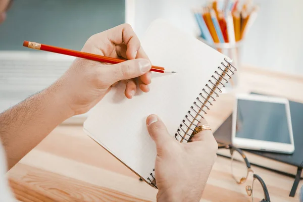 Empresario está planeando una nueva grabación de inicio en un bloc de notas. Manos de hombre sosteniendo un lápiz rojo toman notas en un cuaderno de papel. Concepto de ideas de negocio. Primer plano. Imagen tonificada —  Fotos de Stock