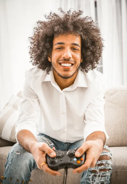 Ευτυχισμένος Άραβας χαμογελάει παίζοντας γενικά το παιχνίδι του υπολογιστή. Shaggy gamer κατέχει Play Station joystick κάθεται σε άνετο καναπέ στο σπίτι. Αστεία ιδέα του χρόνου. Έννοια συναισθημάτων. Τονισμένη εικόνα — Φωτογραφία Αρχείου