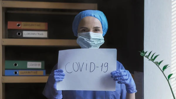 医師は碑文Covid-19を保持している。女性医学保護制服で危険なウイルス発生についてのスローガンを示しています.医療の概念 — ストック写真