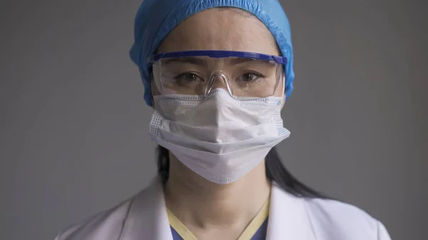 Docteur en lunettes de sécurité et masque. Portrait de femme asiatique en uniforme médical et lunettes regardant la caméra sur fond gris — Photo