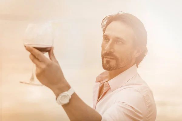 Homem caucasiano segura um copo de vinho tinto. silhueta masculina com vinho em ensolarado de volta iluminado. Conceito de degustação. Imagem tonificada — Fotografia de Stock