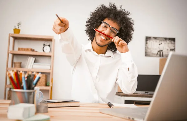 Studente felice divertirsi durante la pausa lavoro. Giovane uomo arabo in camicia bianca ampiamente sorride e gesti che tengono le matite in mano. Immagine tonica — Foto Stock