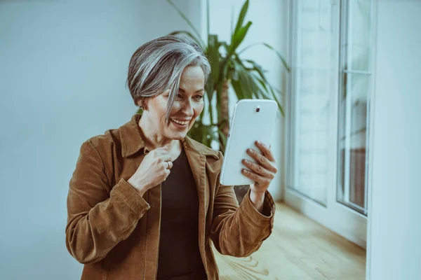 Wanita berambut perak ceria berkomunikasi secara online pada tablet digital. Cantik wanita dewasa tersenyum memiliki pertemuan online dengan orang-orang yang indah tinggal di rumah. Citra cetak — Stok Foto