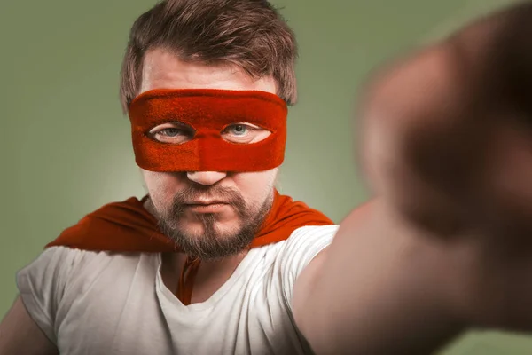 Super héroe hombre hace selfie fotos o vídeo por los teléfonos móviles. Hombre serio con máscara roja y capa posando para sus seguidores en las redes sociales. Aislado sobre fondo verde — Foto de Stock