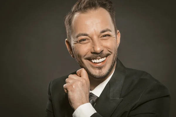 Cheerful businessman smiles broadly touching his beard and looking at camera. Close up portrait of Caucasian handsome man in formalwear. Toned image — Stock Photo, Image