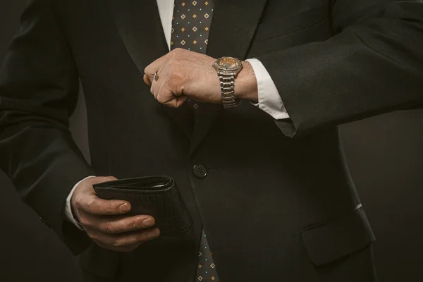 El hombre de negocios comprueba el tiempo mirando un reloj de pulsera con una billetera de cuero cara en la mano. Primer plano. Concepto de fecha límite. Imagen tonificada — Foto de Stock