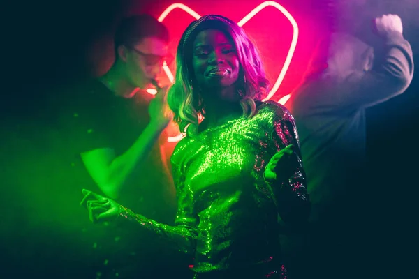 Sexy mujer afroamericana bailando en colores brillantes de neón iluminación de club nocturno. Mujer joven y multitud de personas que se divierten en la discoteca de noche —  Fotos de Stock