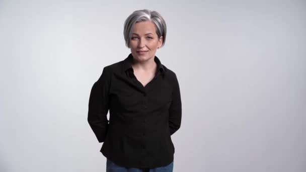 Hübsche erwachsene Frau mit grauen Haaren, die im Studio vor weißem Hintergrund für Fotografen posiert, in lässiger Kleidung, schwarzem Hemd und Jeans. Prores 422 — Stockvideo