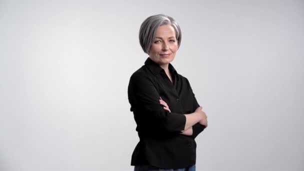 Mujer de pelo gris adulto tipo sensual con los brazos cruzados mostrando expresiones faciales posando para el fotógrafo en el estudio sobre un fondo blanco en ropa casual camisa negra y jeans. Prores 422 — Vídeos de Stock