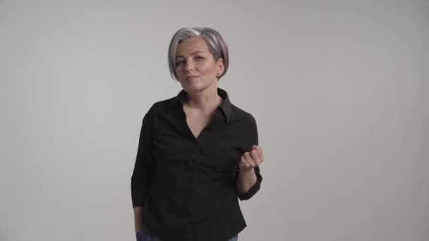 Leichtgläubige reife Frau mit grauen Haaren, die für Fotografen im Studio vor weißem Hintergrund posiert, in lässiger Kleidung, schwarzem Hemd und Jeans. Prores 422 — Stockvideo