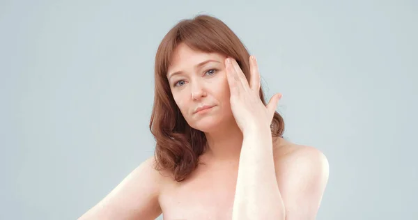 Mature naked woman feels headache. Serious red haired lady touches her head with hand. Skin care concept — Stock Photo, Image