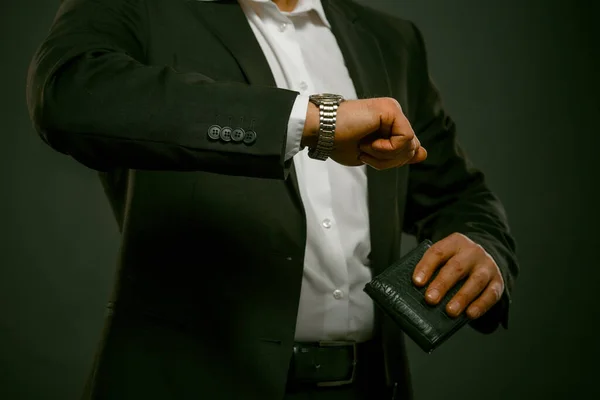 Empresário verificando o tempo em seu relógio de pulso enquanto segurava a bolsa preta na mão. Homem vestindo camisa branca e terno preto olha para relógio de mão. Um tiro de perto. Imagem matizada — Fotografia de Stock