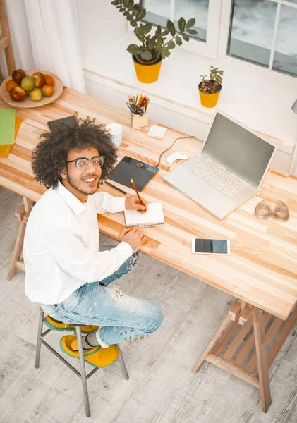 Hombre creativo del milenio que trabaja en el lugar de trabajo en casa. El joven empresario árabe mira a la cámara sentada en un escritorio de madera con computadora, teléfono móvil y tableta gráfica. Vista de ángulo alto. Imagen teñida — Foto de Stock