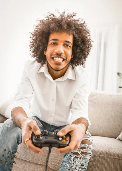 Jovem jogando jogo de computador sozinho em casa. Shuggy gamer sorri segurando joystick. Conceito de auto-isolamento. Ângulo holandês, vista frontal. Conceito de emoções. Imagem matizada — Fotografia de Stock