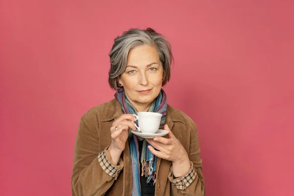 Очаровательная белая женщина пьет кофе с белой чашкой. Довольно зрелая леди улыбается слегка изолированно на розовом фоне. Концепция красоты. Концепция кофе — стоковое фото