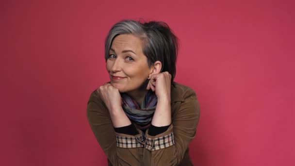 Stylish graying Woman charmingly smiles looking at camera. Caucasian mid aged dressed in brown corduroy jacket with multi-colored scarf touches her face with hand. prores 422 — Stock Video