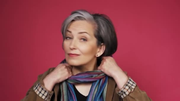 Mature gray haired freelancer woman correcting her scarf by hands creative woman making fun posing on a pink background. Prores 422 — Stock Video