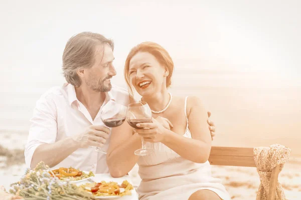 Mujer madura y hombre felices juntos. Pareja amorosa se miran abrazando y beber vino tinto citas en la cafetería de la playa. Concepto de brindis festivo. Imagen teñida —  Fotos de Stock