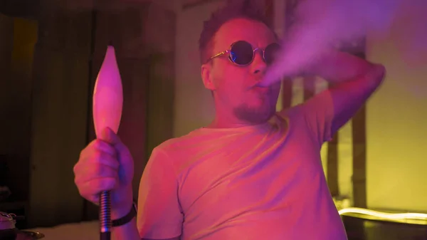 Man andas ut rök i neon bakgrundsbelyst. Vit man i solglasögon rökning hookah hemma mot usa flagga bakgrund. Viloprincip — Stockfoto