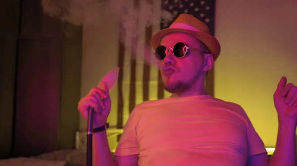 Hipster człowiek palący hookah i dansing w jasnym świetle neonów kolorów. śmieszne palacz gospodarstwa shisha rura to zabawy sam w ciemnym pokoju — Zdjęcie stockowe