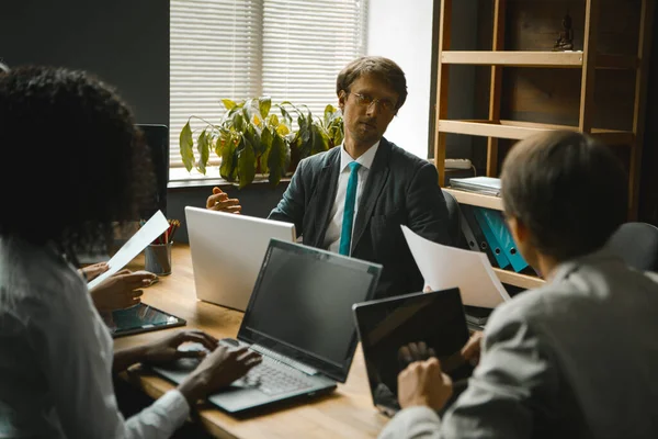 Équipe d'affaires travaillant ensemble assis à la table du bureau. Concentration sélective sur l'homme d'affaires coûteux dans les lunettes pensant près de la fenêtre. Travail d'équipe du personnel de bureau. Image tonique — Photo