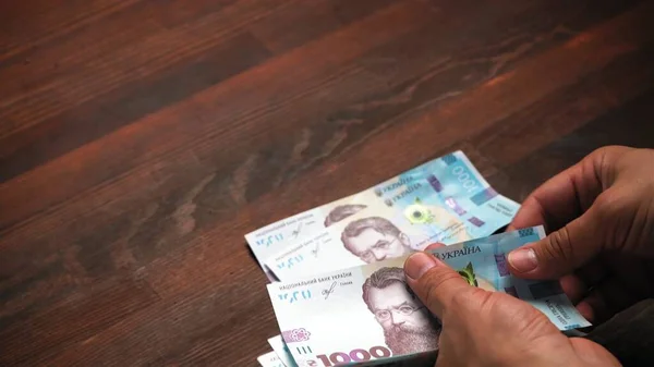 Man denkt über neues ukrainisches Papiergeld nach. Er sieht zum ersten Mal neue Scheine im Nennwert von 1000 Griwna. Konzentrieren Sie sich auf die Hände im Vordergrund. Textfeld auf der linken Seite. Inflationskonzept. Austauschkonzept — Stockfoto