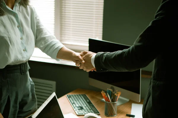 握手だ。男性と女性の手を閉じて、現代のオフィスの職場を背景に揺れ合います。緑の色合いの画像 — ストック写真
