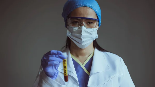 Assistente de laboratório segura tubo de teste com sangue em primeiro plano azul. Trabalhadora do laboratório médico isolada no fundo cinzento. Um tiro de perto. Imagem tonificada — Fotografia de Stock