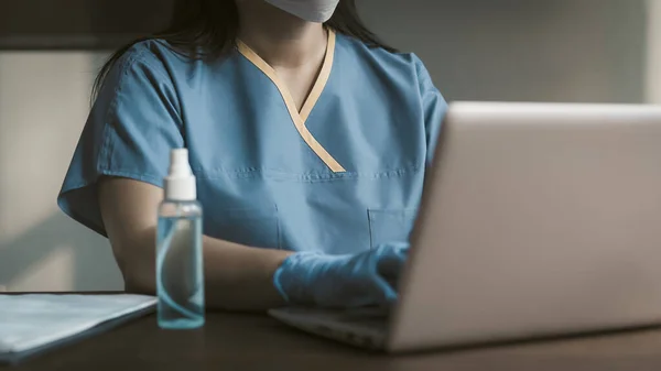 Framifrån på sjuksköterska eller läkare som använder bärbar dator. Kvinna i blå arbetskläder som skriver på datorns tangentbord. Närbild skott. Tonad bild — Stockfoto