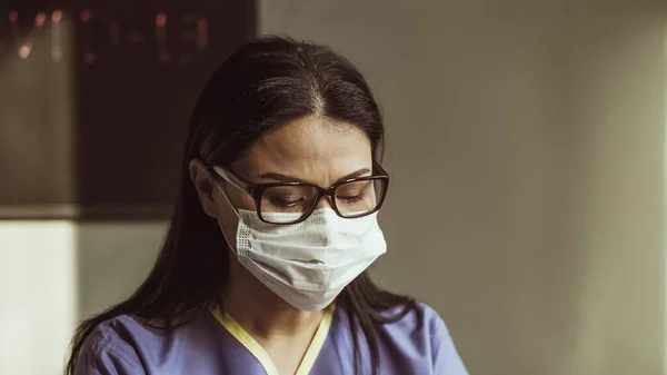 Portretul unei femei obosite, cu masca de protectie si ochelari, privind in jos. Doctorul foloseşte laptopul în biroul ei. Împuşcat de aproape. Imagine tonată — Fotografie, imagine de stoc