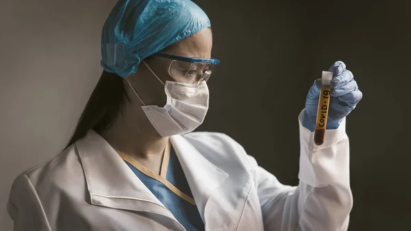Medicul se uită la tubul de testare cu sânge de Covid 19 coronavirus infectat. Un lucrător medical de laborator serios care o examinează pregătindu-se pentru teste de vaccin. Lovitură de aproape. Imagine tonată — Fotografie, imagine de stoc