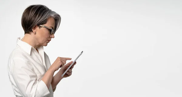 Femme d'affaires caucasienne aux cheveux gris tapant sur tablette sur fond blanc. Modèle horizontal pour bannière publicitaire avec textspase à droite — Photo